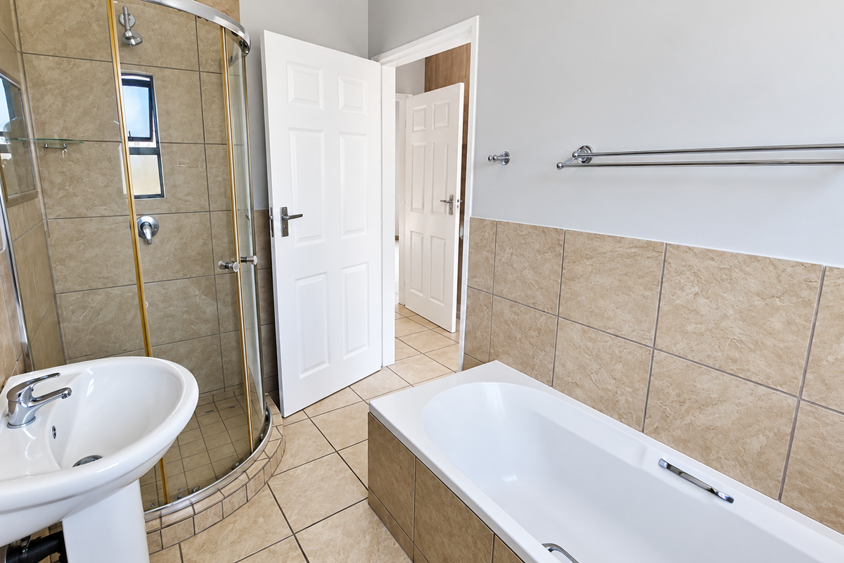 A clean, functional bathroom featuring a pedestal basin, a curved glass shower enclosure, and a built-in bathtub with neutral ceramic wall and floor tiles.