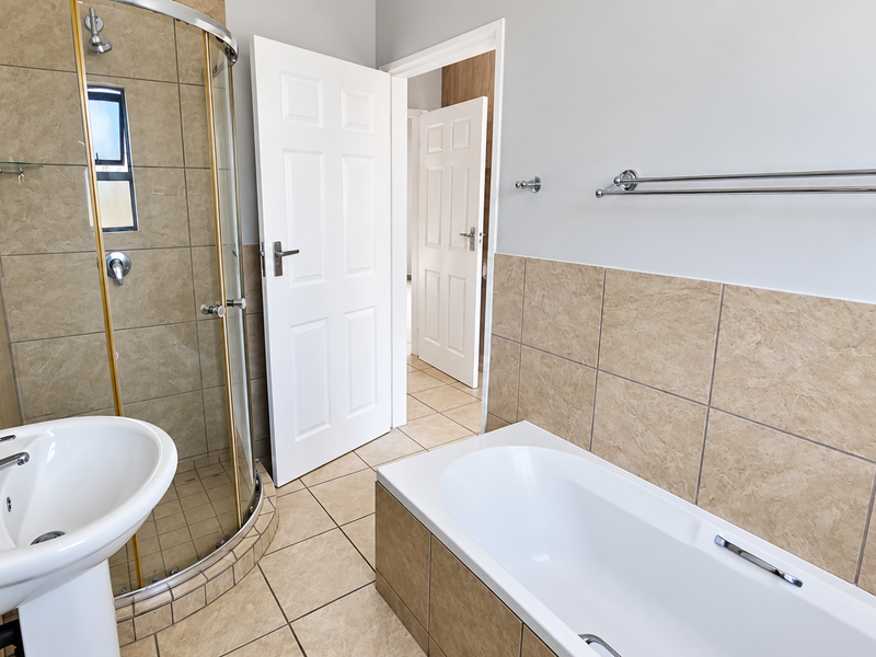 A clean, functional bathroom featuring a pedestal basin, a curved glass shower enclosure, and a built-in bathtub with neutral ceramic wall and floor tiles.