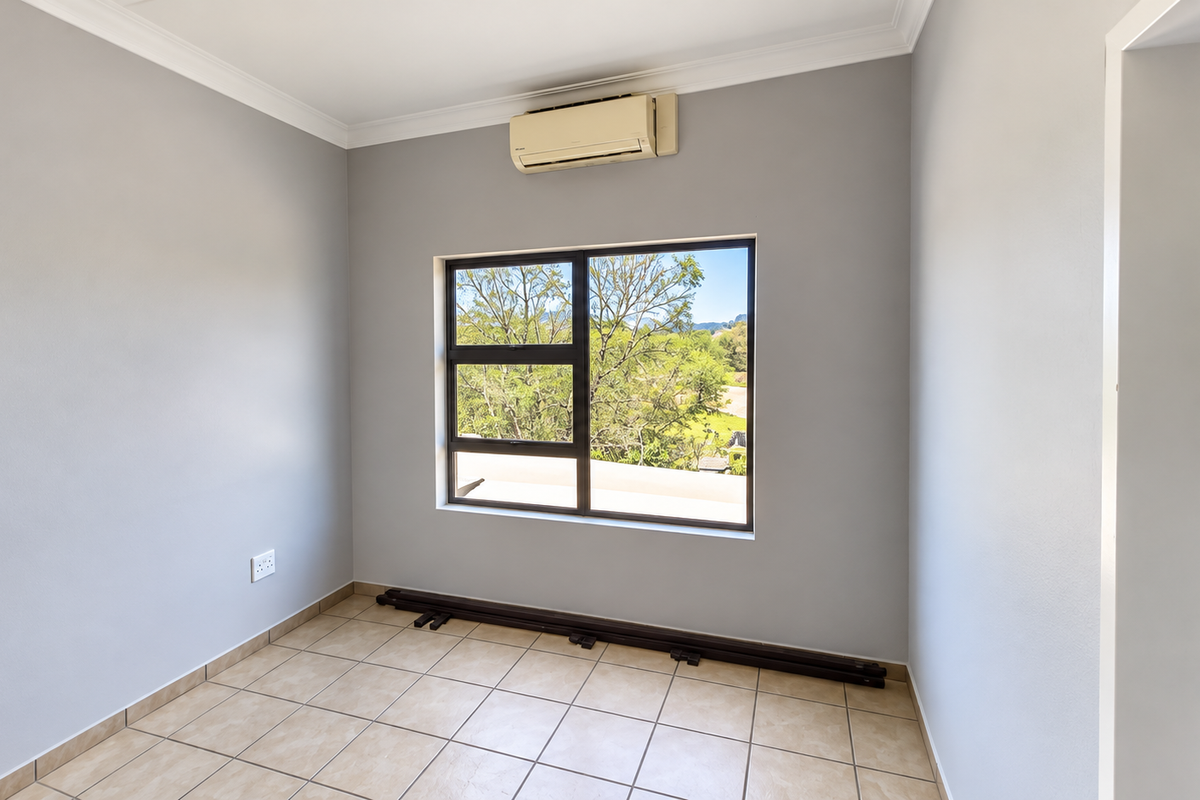 A bright, empty bedroom featuring tiled flooring, a wall-mounted air conditioning unit, and a large window with views of the surrounding greenery.
