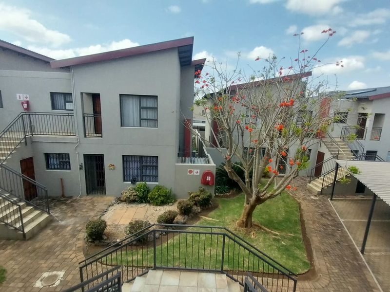 An elevated view of a residential apartment complex courtyard featuring paved walkways, metal staircases, a carport, and landscaped garden areas.