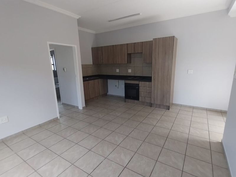 An open-plan living and kitchen area featuring tiled flooring, modern wood-finish cabinetry, and a built-in oven and hob.