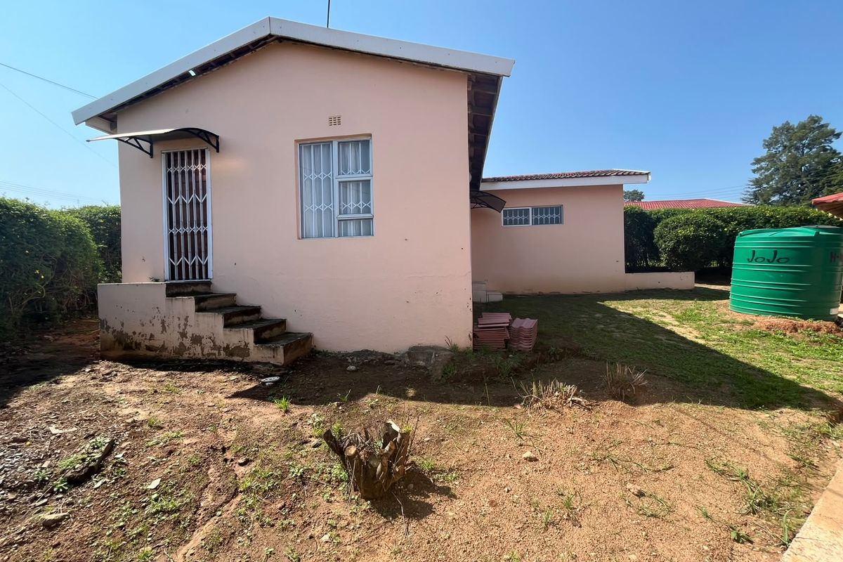 Rear view of the property featuring a pink exterior facade, security gates, concrete steps, and a green water storage tank in the garden area.
