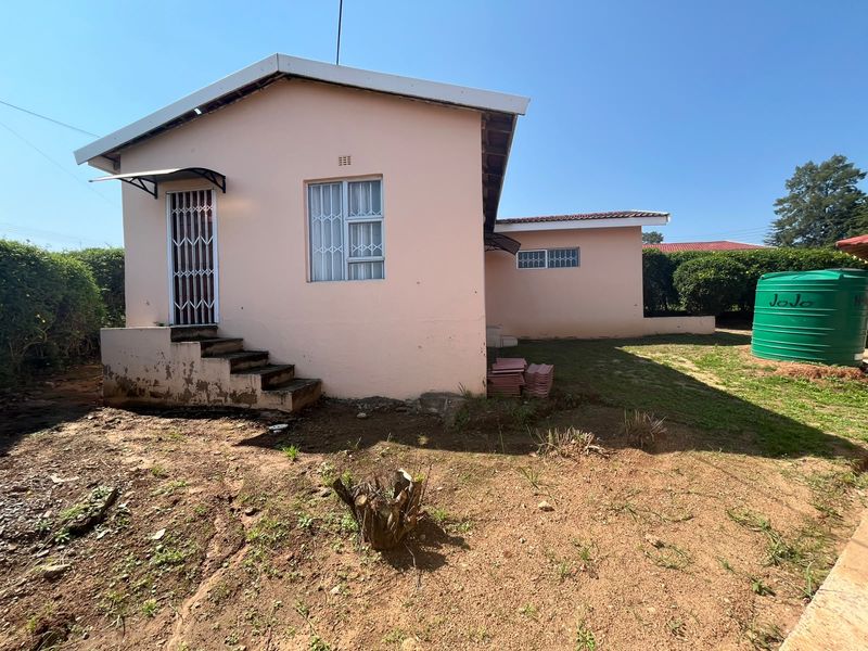Rear view of the property featuring a pink exterior facade, security gates, concrete steps, and a green water storage tank in the garden area.