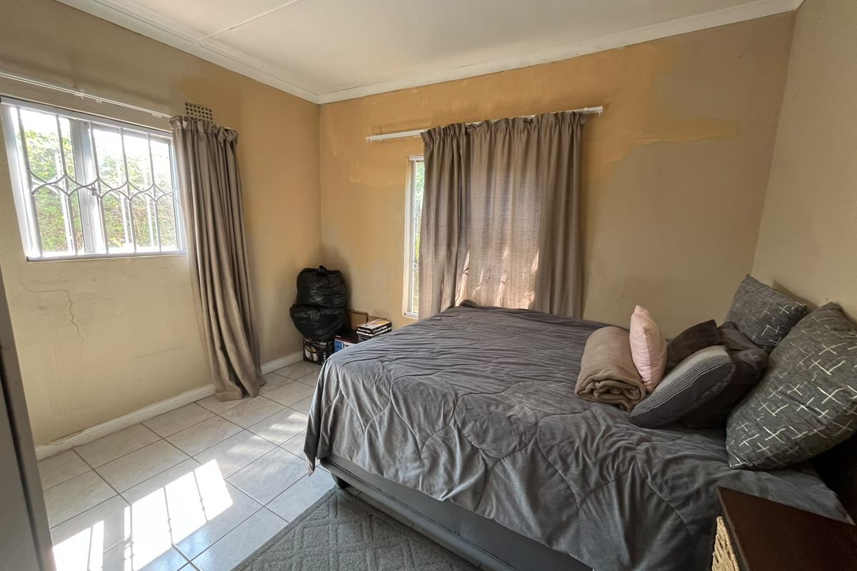 A bedroom featuring tiled flooring and security bars on the windows, currently requiring wall repairs and repainting to improve its overall condition.