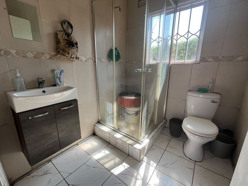 A functional bathroom featuring a vanity cabinet, a glass-enclosed shower, and a toilet, finished with tiled walls and flooring.