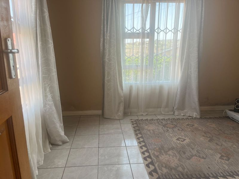 A bright, tiled living area featuring a window with security bars and neutral wall tones, offering a clean, blank canvas for interior design.