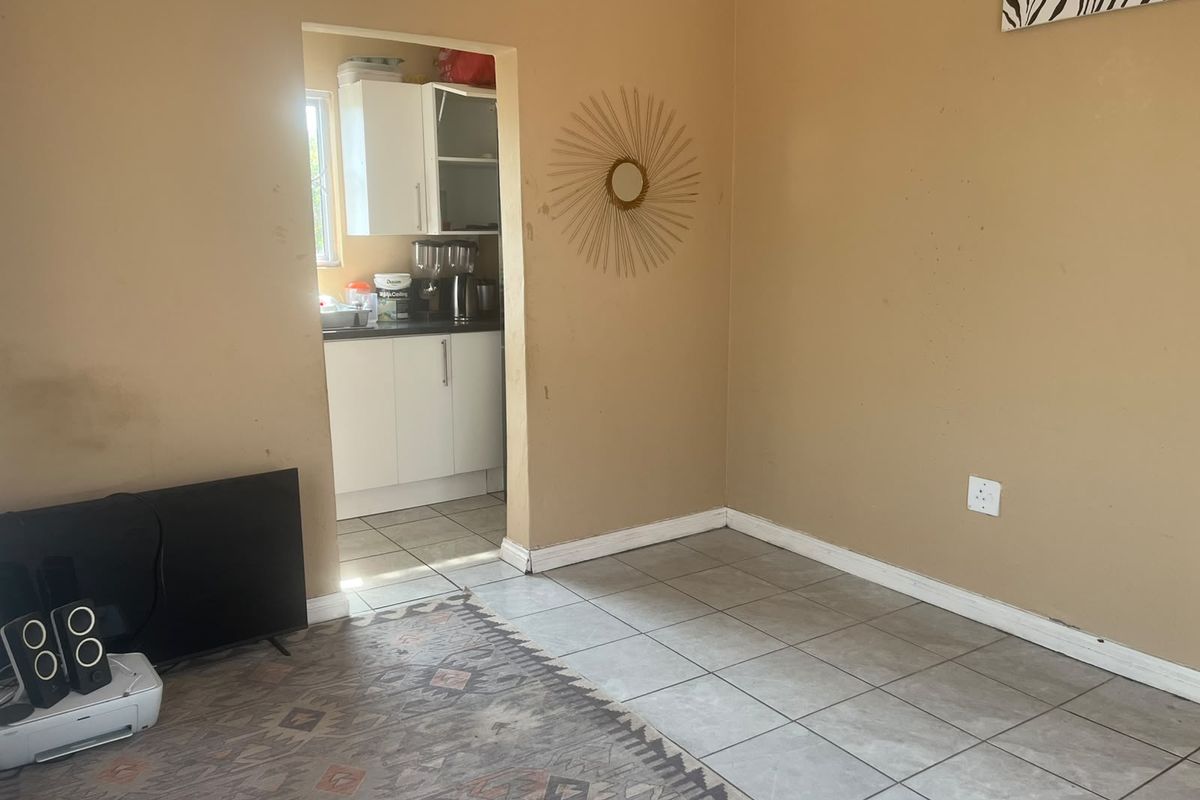 A living room area with tiled flooring and neutral wall paint, featuring an open doorway leading into a kitchen space.