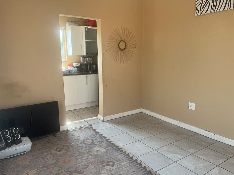 A living room area with tiled flooring and neutral wall paint, featuring an open doorway leading into a kitchen space.