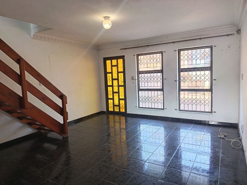 An empty living room featuring dark tiled flooring, a wooden staircase, and security-fitted windows and door.