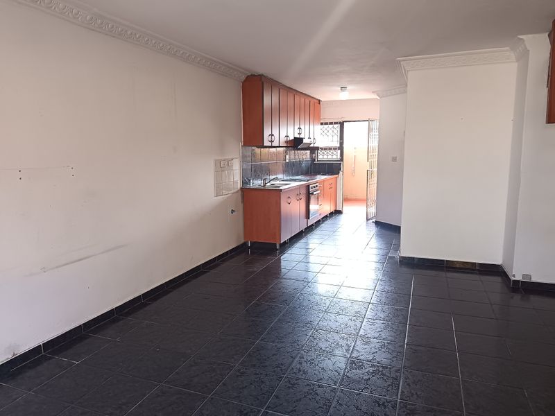 An empty kitchen featuring dark tiled flooring, wooden cabinetry, built-in oven and hob, with direct access to an outdoor area through a security gate.
