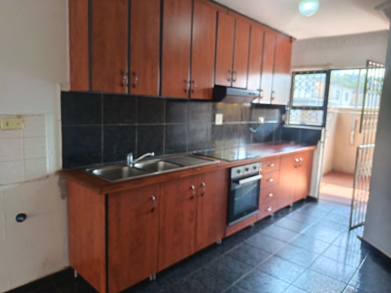 A functional kitchen featuring wooden cabinetry, a built-in oven, hob, and extractor fan, with direct access to an outdoor area.