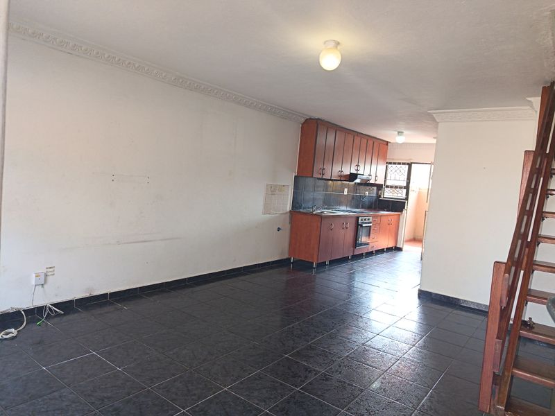 Open-plan living and kitchen area featuring dark tiled flooring, wooden cabinetry, integrated oven, and a staircase leading to the upper level.