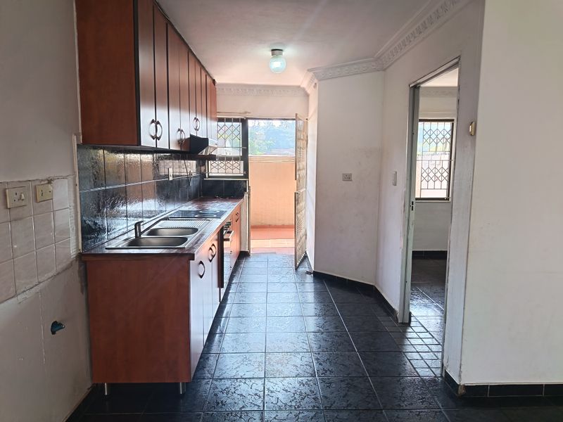 A functional kitchen featuring dark tiled flooring, built-in wooden cabinetry, and direct access to an outdoor balcony area.