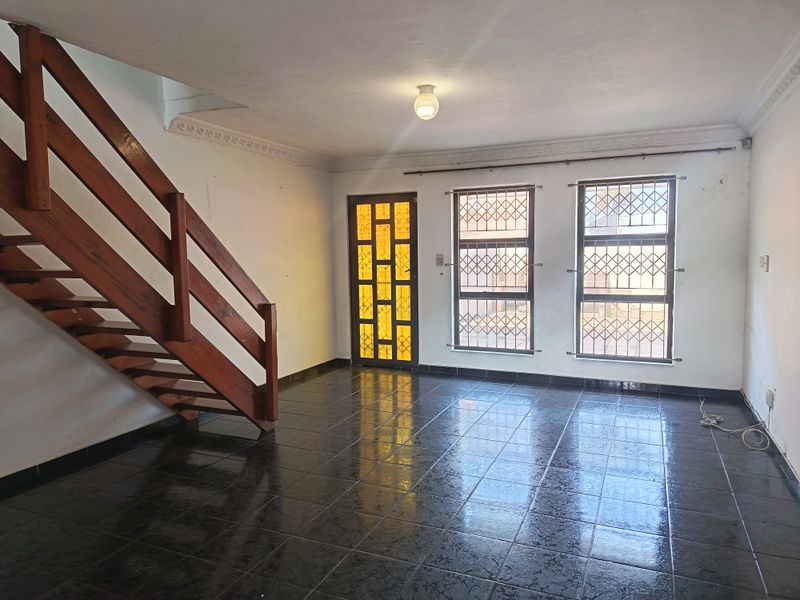 An open-plan living area featuring dark tiled flooring, a wooden staircase, and security-fitted windows and doors.