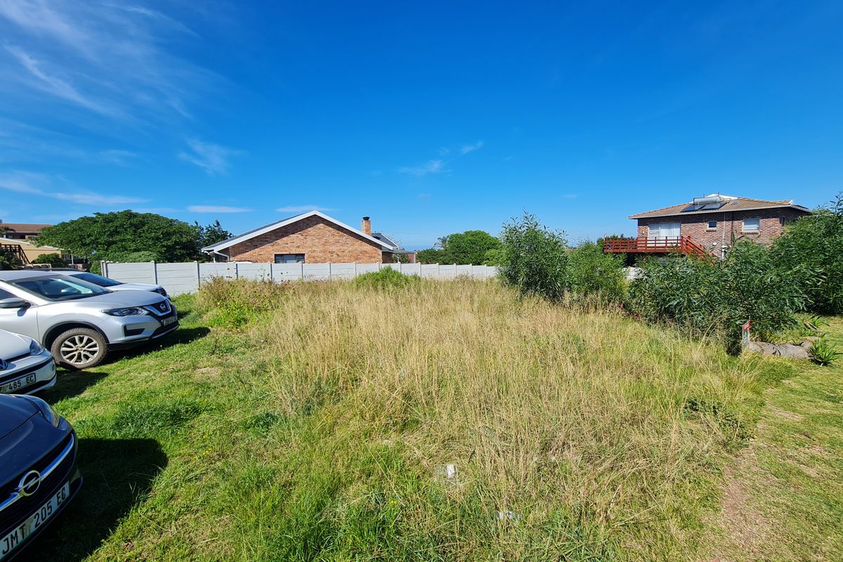 A vacant residential plot featuring overgrown grass and a precast concrete boundary wall, situated in a developed neighborhood.