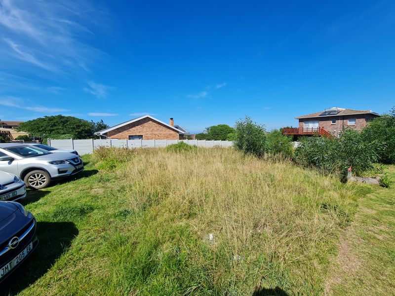 A vacant residential plot featuring overgrown grass and a precast concrete boundary wall, situated in a developed neighborhood.