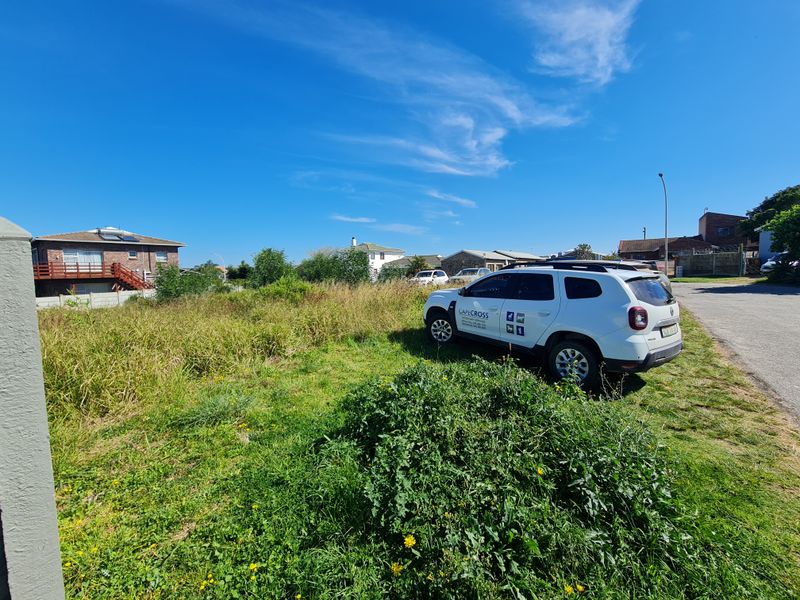 A view of a vacant residential plot featuring overgrown grass, situated in a developed neighborhood.