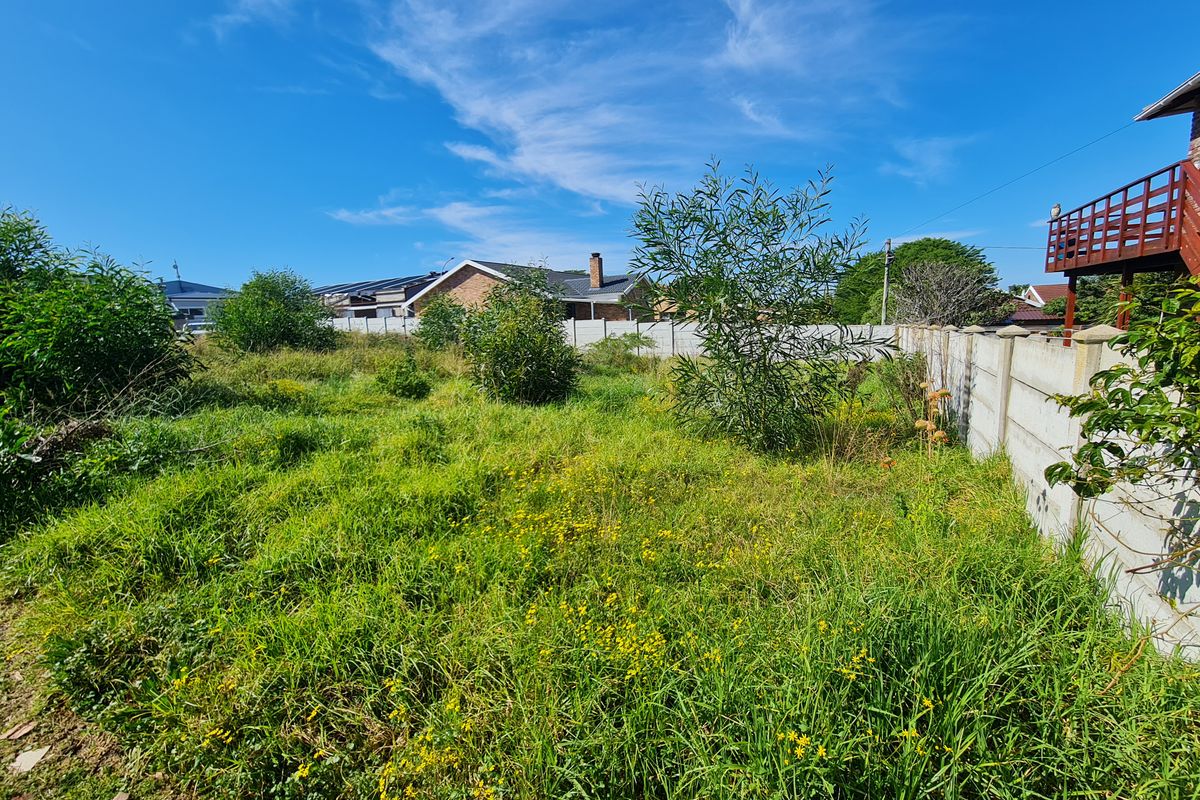 A view of a vacant residential plot featuring overgrown grass and a precast concrete boundary wall.