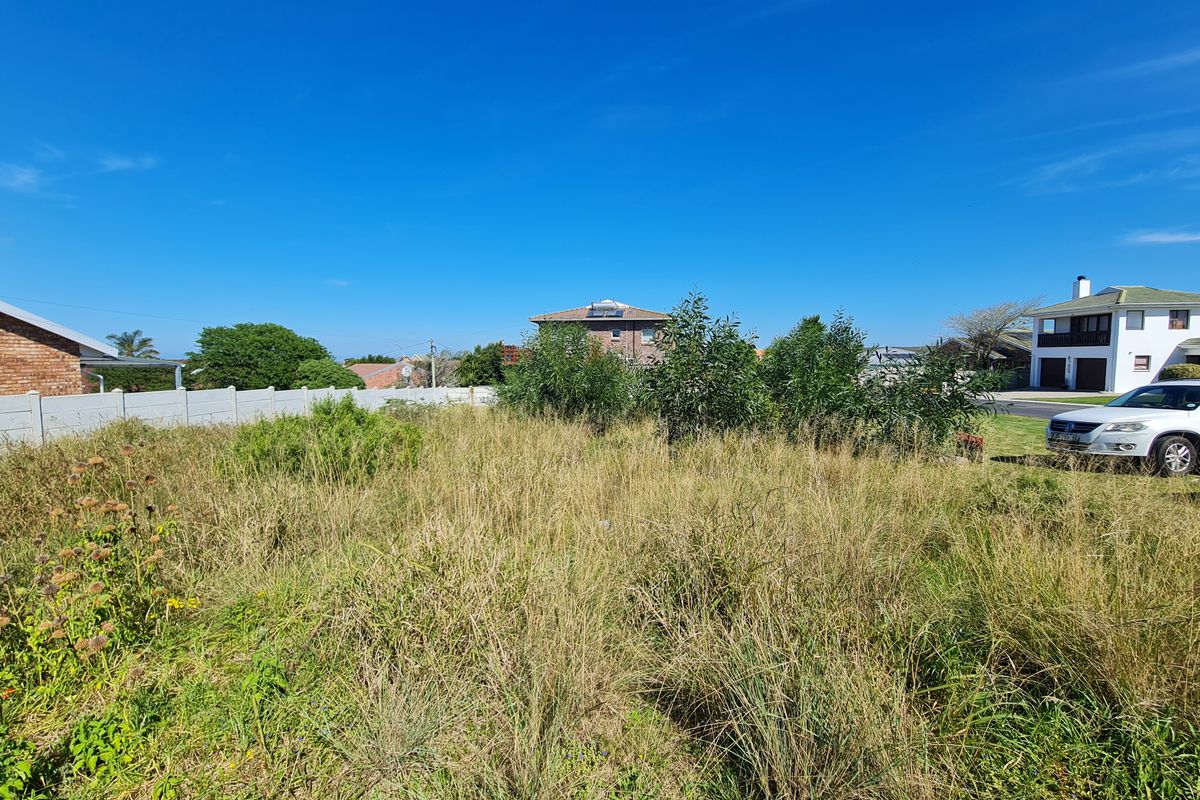 A vacant residential plot featuring overgrown grass and a precast concrete boundary wall, situated in a developed neighborhood.