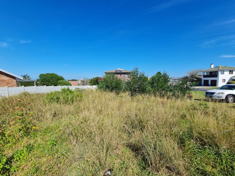 A vacant residential plot featuring overgrown grass and a precast concrete boundary wall, situated in a developed neighborhood.