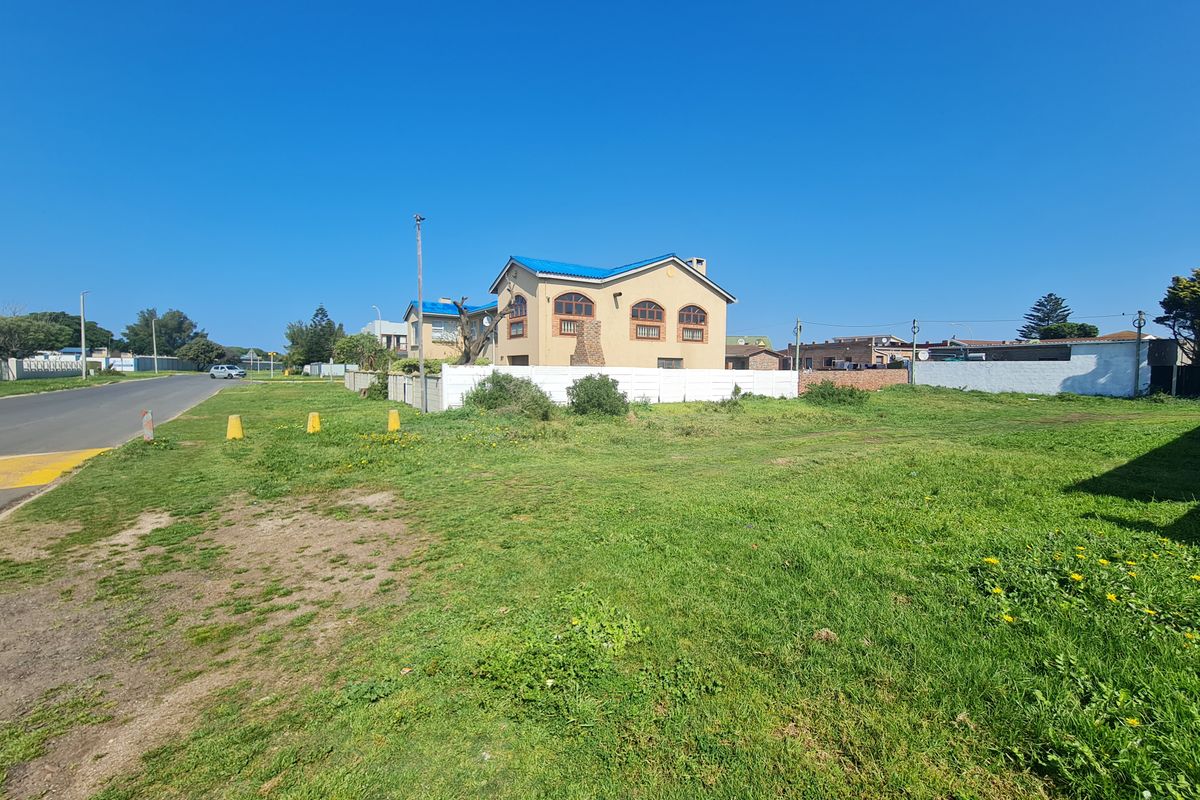 A vacant residential plot of land featuring a grass lawn and boundary wall, situated in a suburban street setting.