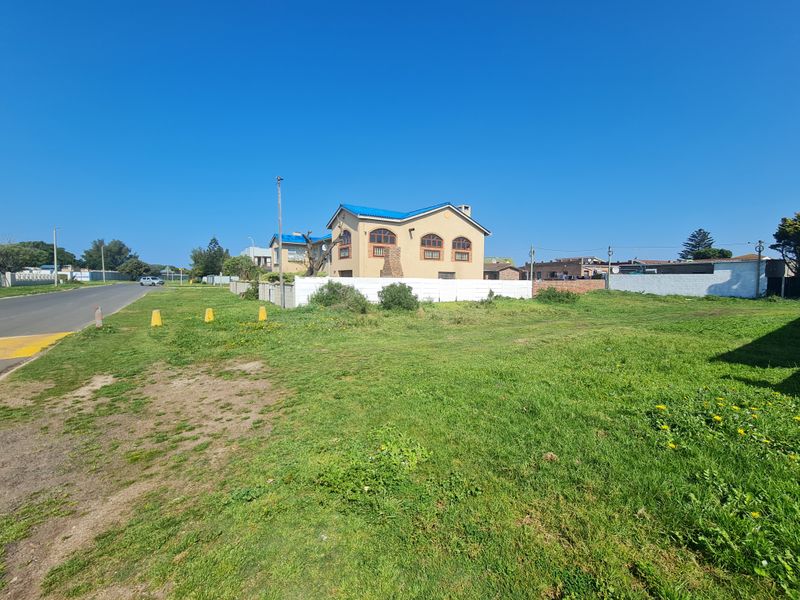 A vacant residential plot of land featuring a grass lawn and boundary wall, situated in a suburban street setting.