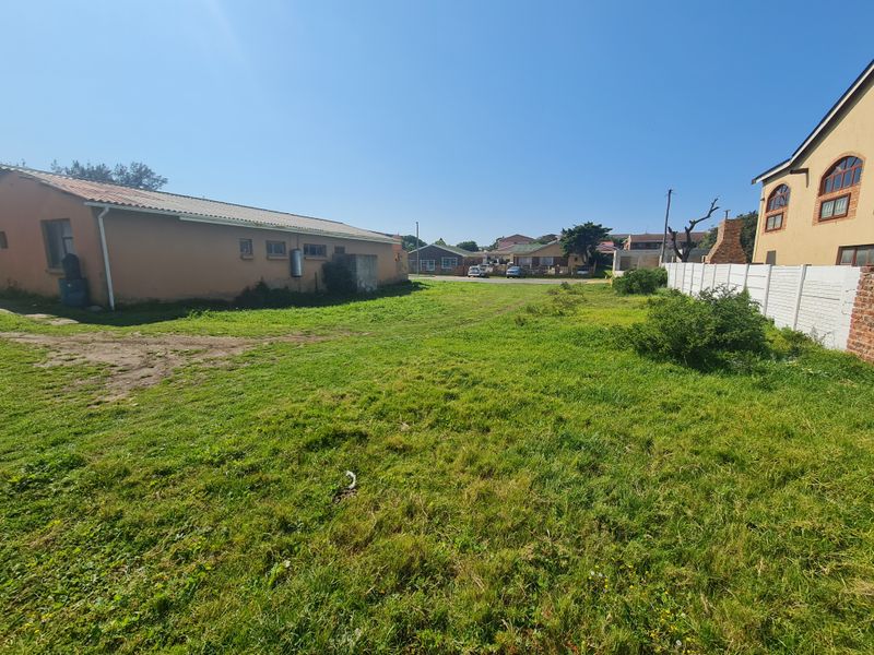 A view of the rear yard area featuring a grass lawn, boundary wall, and adjacent residential structures.