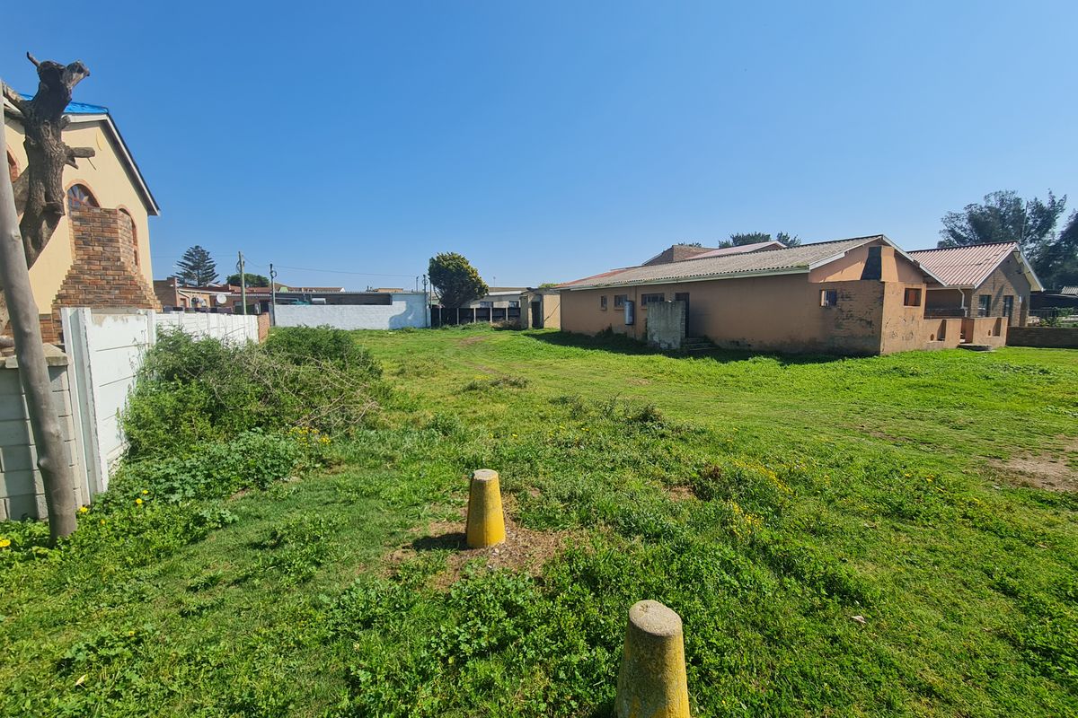 A view of the rear yard area featuring a large grassed plot, concrete boundary walling, and existing residential structures on the adjacent properties.