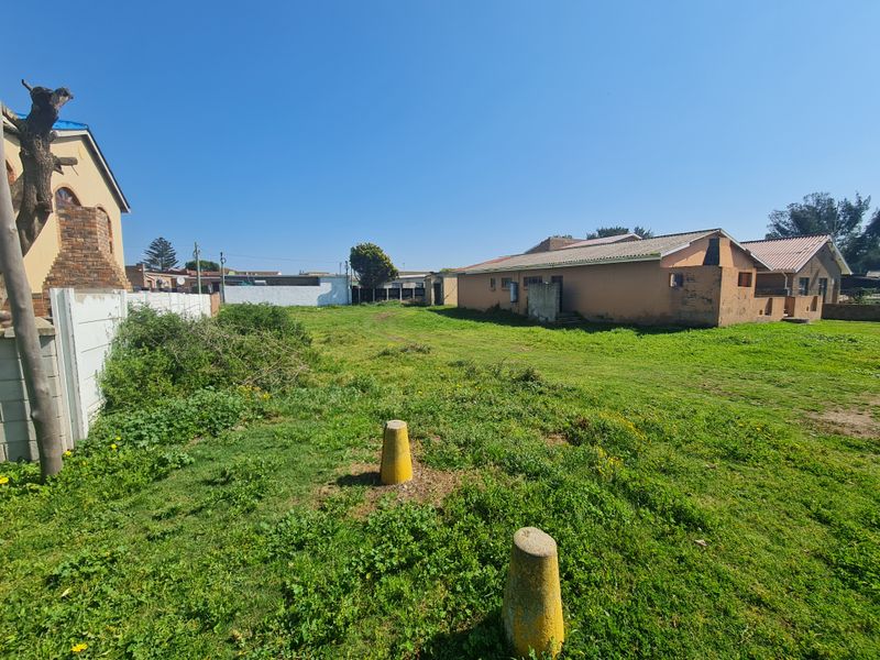 A view of the rear yard area featuring a large grassed plot, concrete boundary walling, and existing residential structures on the adjacent properties.