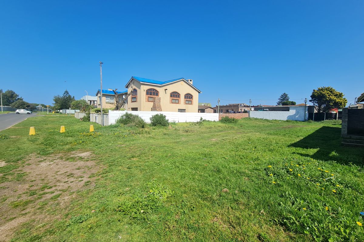A view of a vacant residential plot featuring a grass lawn and boundary wall, with neighboring properties visible in the background.