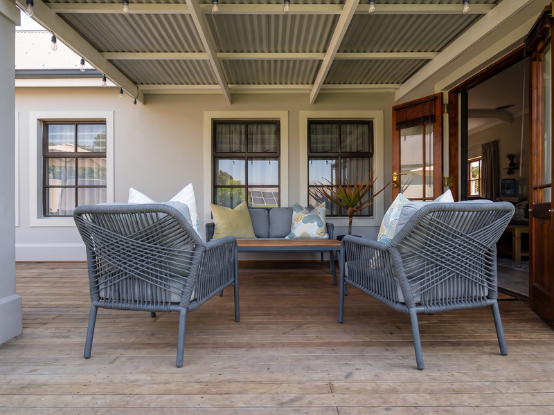A covered outdoor patio featuring timber decking, a corrugated metal roof, and direct access to the interior through timber-framed glass doors.