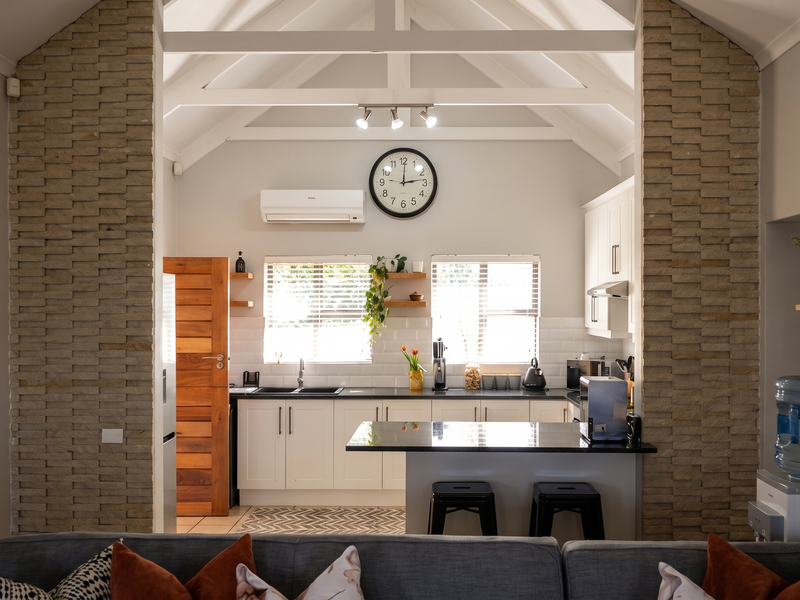 Open-plan kitchen featuring vaulted ceilings with exposed trusses, stone feature walls, modern cabinetry, and a central island with granite countertops.
