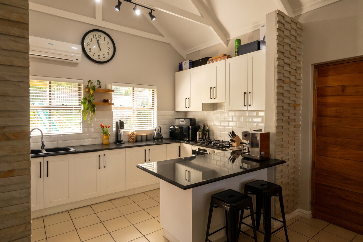 Modern kitchen featuring white cabinetry, granite countertops, subway tile backsplash, gas hob, and a striking stone feature wall under a vaulted ceiling.
