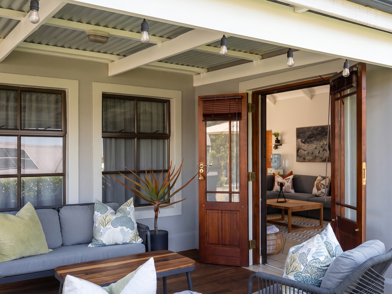 A covered patio area featuring timber decking, timber-framed doors and windows, and overhead pendant lighting, providing a seamless transition to the interior living space.
