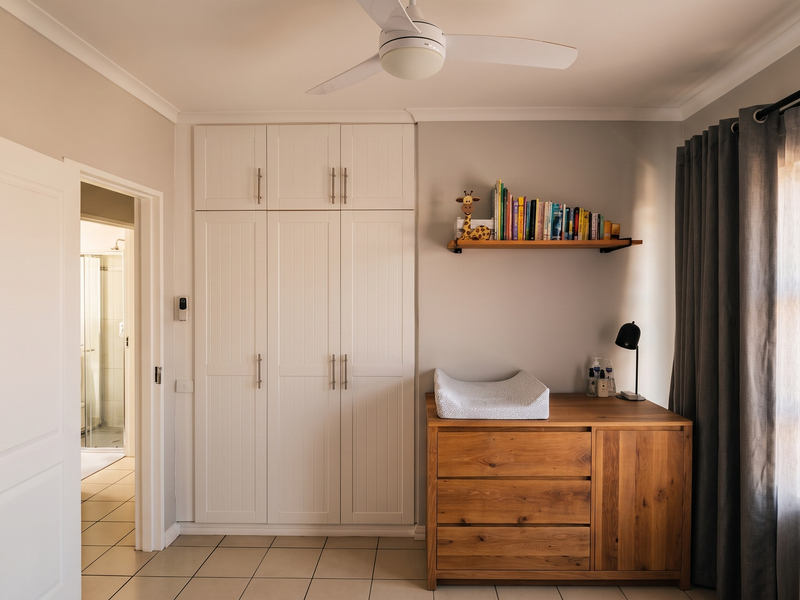 A well-maintained bedroom featuring built-in cupboards, a ceiling fan, and tiled flooring, with direct access to an adjacent bathroom.