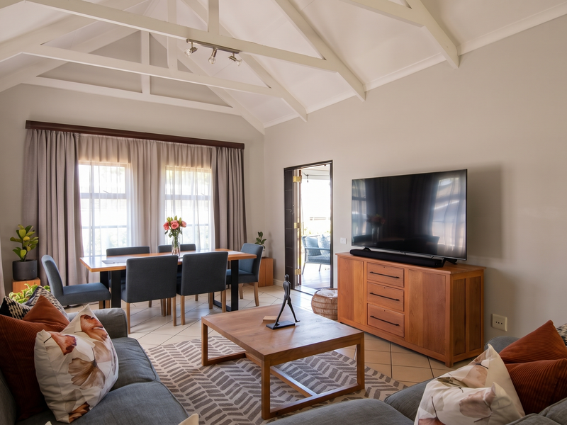 Spacious open-plan living and dining area featuring a high vaulted ceiling with exposed trusses, tiled flooring, and direct access to an outdoor patio.