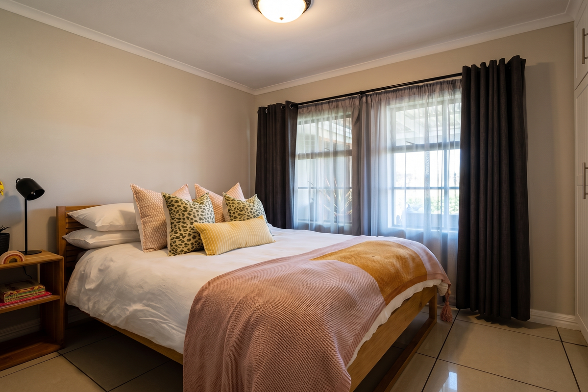 A well-maintained bedroom featuring neutral tiled flooring, ample built-in cupboard storage, and natural light through a window with security bars.