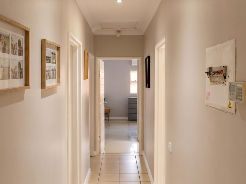 A clean, well-lit hallway featuring tiled flooring, a ceiling access hatch, and wall-mounted electrical distribution board and alarm system.