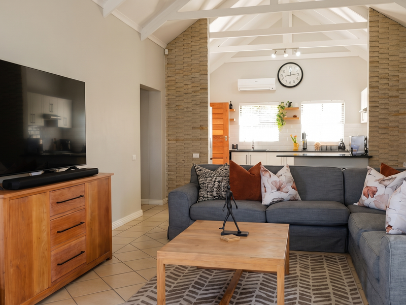 Spacious open-plan living and kitchen area featuring vaulted ceilings with exposed beams, stone feature pillars, and modern tiled flooring.