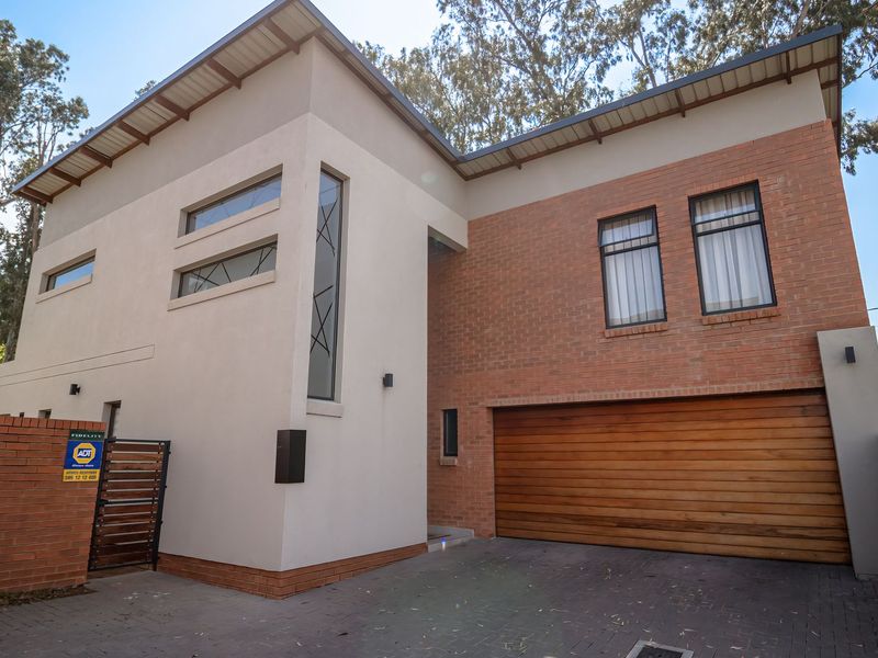 Modern double-story residential facade featuring a combination of brick and plastered finishes, a wooden garage door, and a paved driveway.