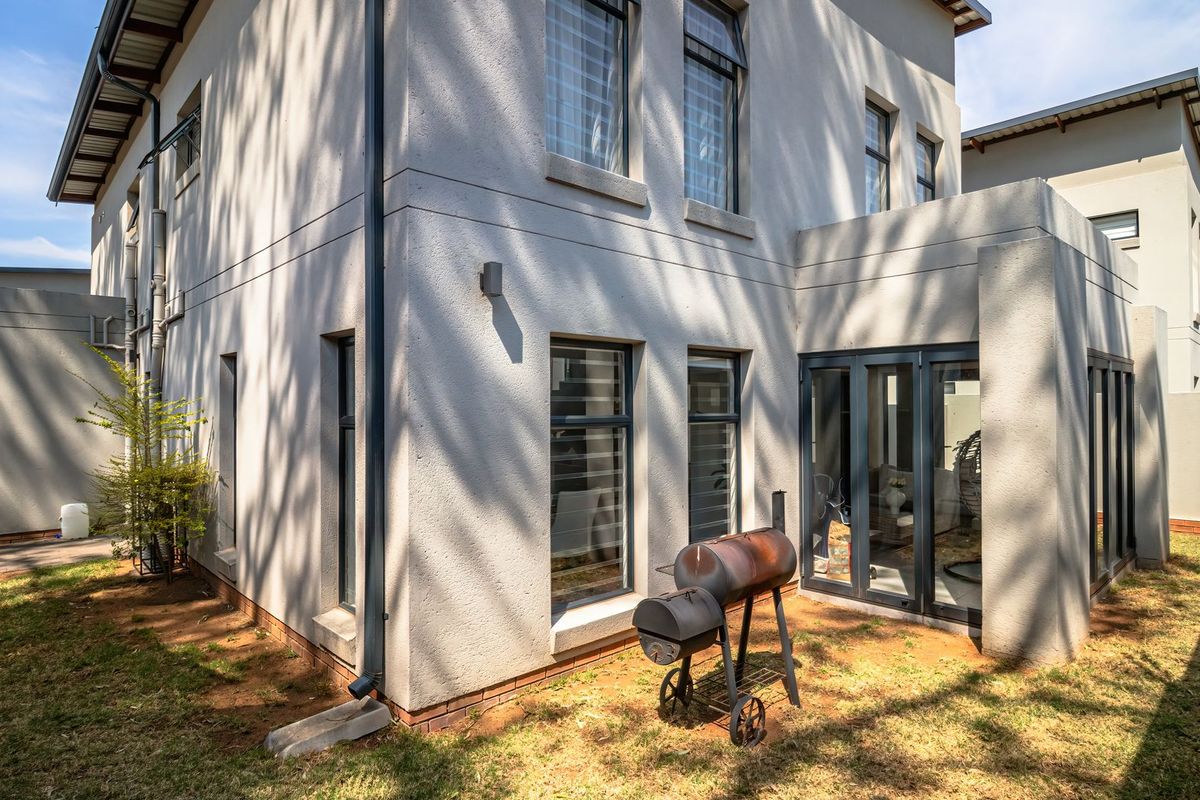 Rear view of the double-story house featuring modern rendered walls, aluminium window frames, and bifold doors leading to the garden area.