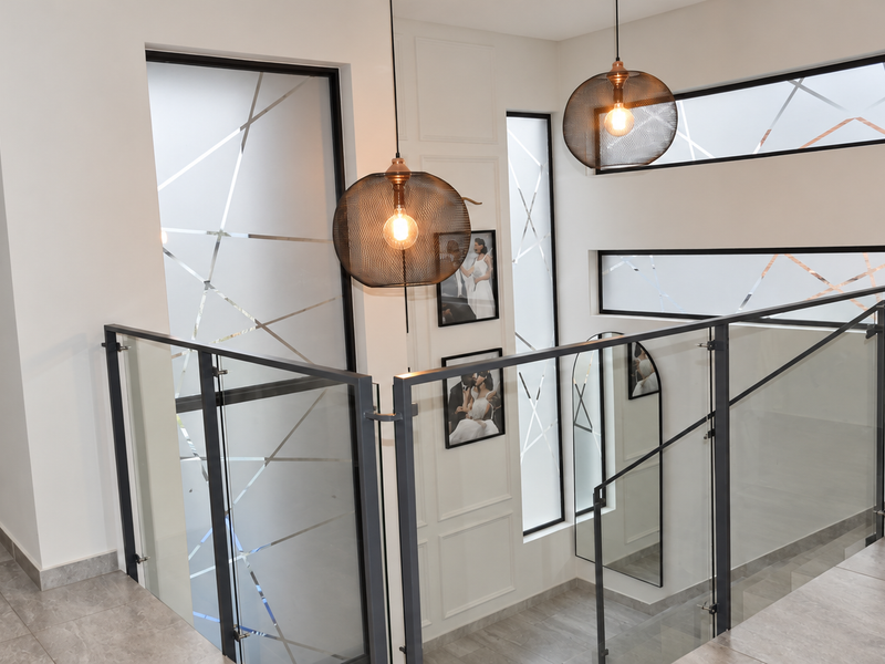 A modern, well-lit hallway featuring a glass balustrade, decorative wall paneling, and stylish pendant lighting with frosted glass windows.