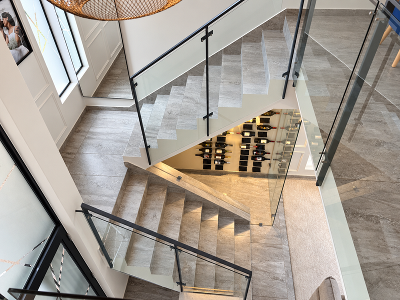 Modern staircase featuring stone treads, glass balustrades, and a sophisticated built-in wine display area, finished with high-quality porcelain floor tiles.