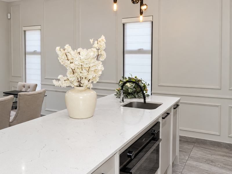 Modern kitchen featuring a stone-topped island with an integrated sink and oven, complemented by elegant wainscoting and neutral tiled flooring.