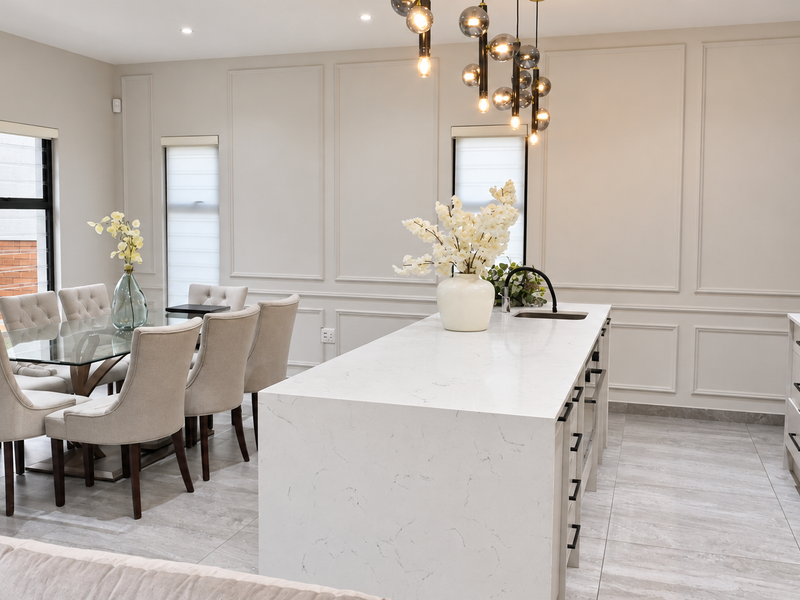 Modern open-plan kitchen and dining area featuring a large quartz island, sleek cabinetry, wainscoting wall detailing, and contemporary pendant lighting.