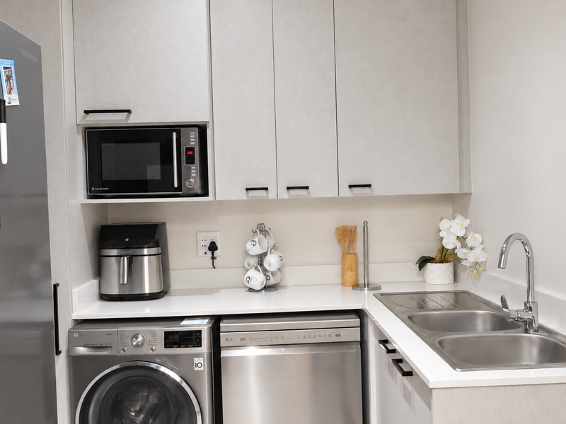 A modern, well-appointed scullery featuring sleek cabinetry, quartz countertops, a double stainless steel sink, and dedicated spaces for laundry and dishwashing appliances.