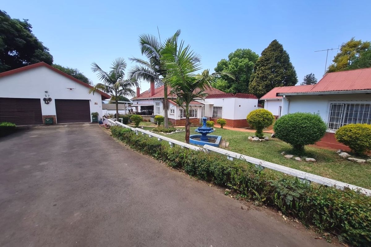 Front view of a residential property featuring a double garage, paved driveway, and a landscaped garden with a central fountain.