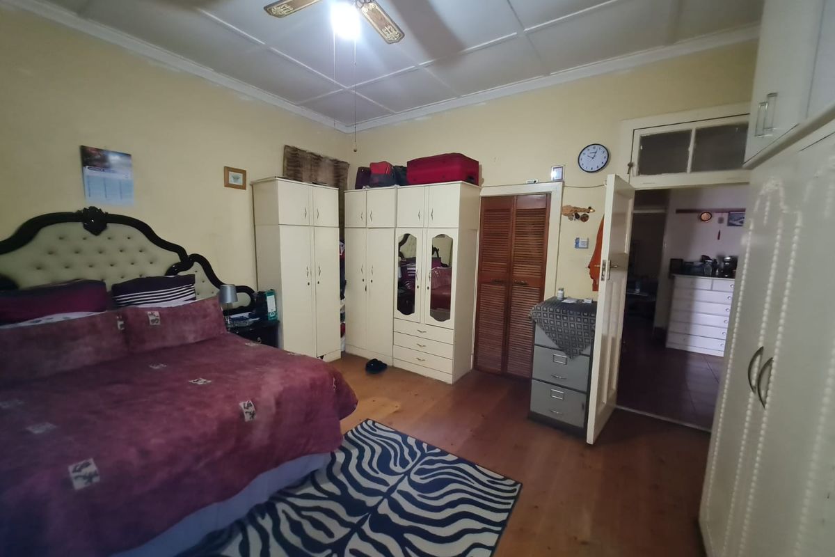 A bedroom featuring wooden flooring, built-in cupboards, and a ceiling fan, with a view into an adjacent room through an open doorway.