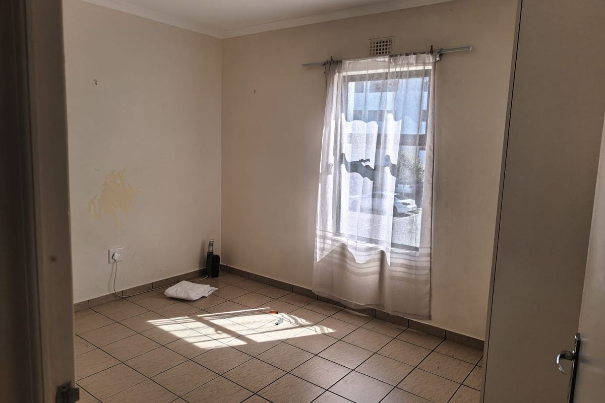 An empty bedroom featuring tiled flooring and a window, requiring minor cosmetic updates such as wall repairs and fresh paint to enhance its appeal.