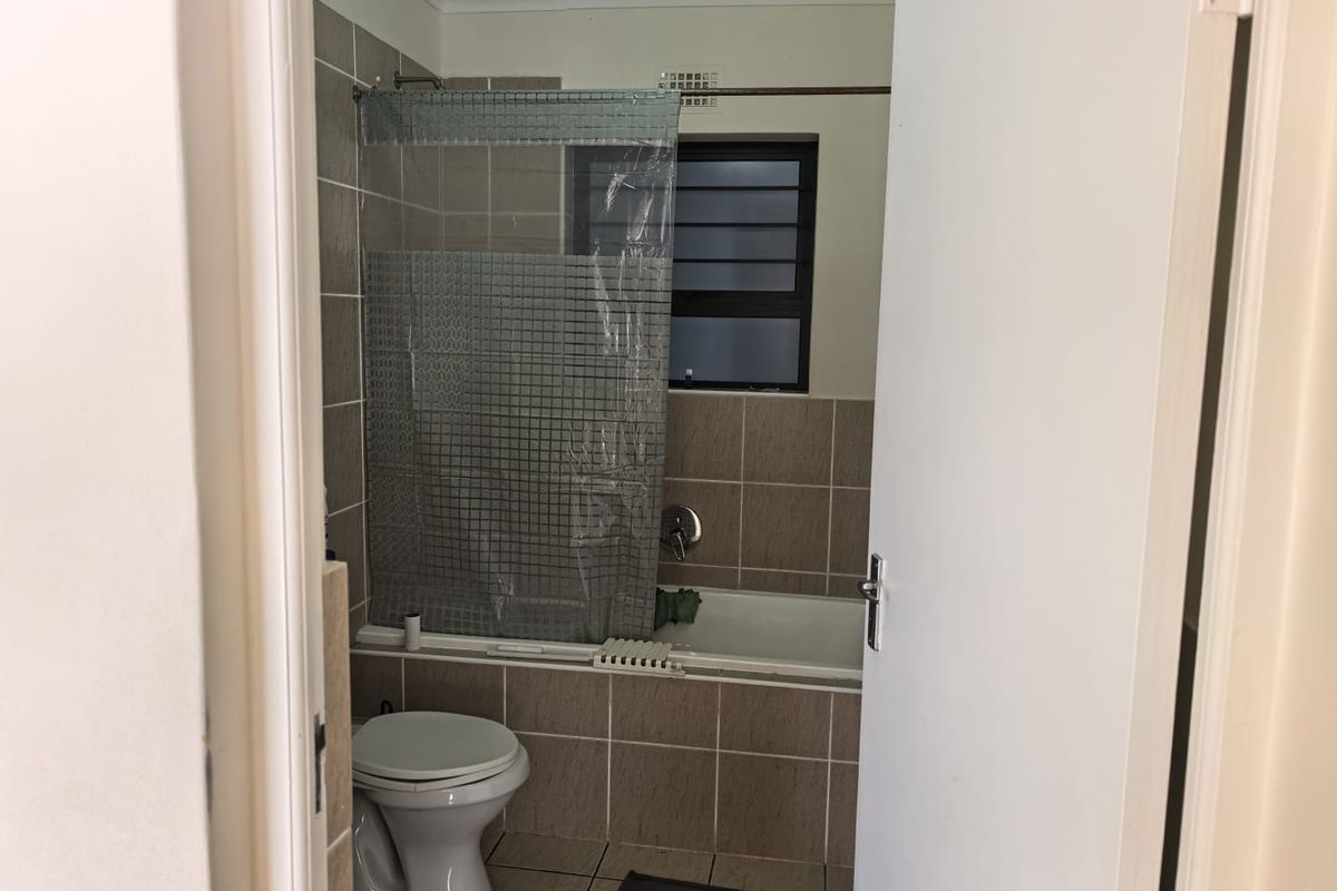 A functional bathroom featuring a bathtub with shower mixer, tiled walls and flooring, and a louvered window for ventilation.